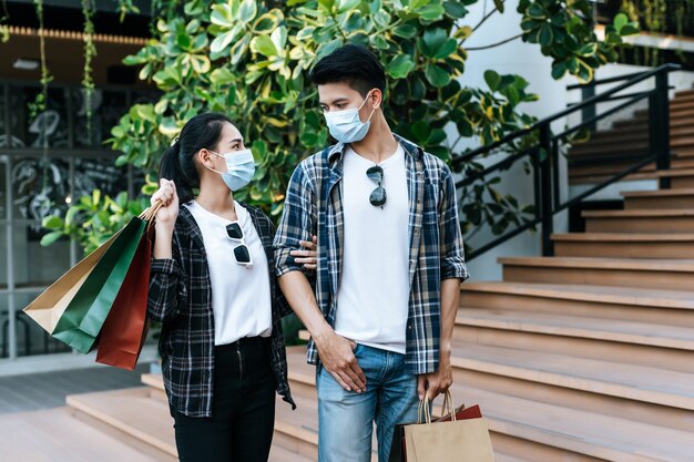 Jeune couple en masque de protection tenant plusieurs sacs en papier