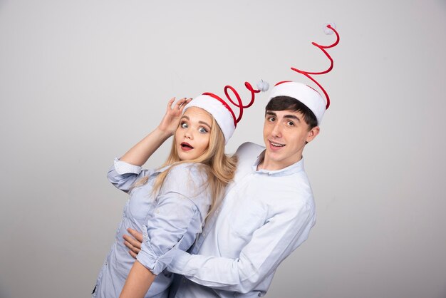 Un jeune couple mignon debout dans un chapeau de Noël et regardant la caméra