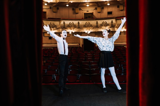 Photo gratuite jeune couple de mime debout sur scène en levant les bras