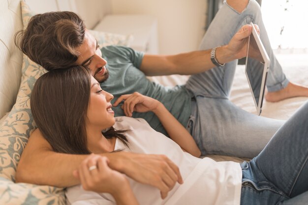 Jeune couple parcourant la tablette sur le lit