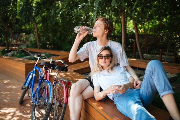 Jeune couple, passer du temps sur un banc en bois dans un parc avec deux vélos à proximité