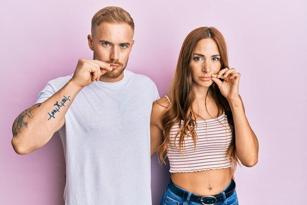 Photo gratuite jeune couple de petite amie et petit ami étreignant et debout ensemble la bouche et les lèvres fermées comme une fermeture éclair avec les doigts. secret et silencieux, parler tabou