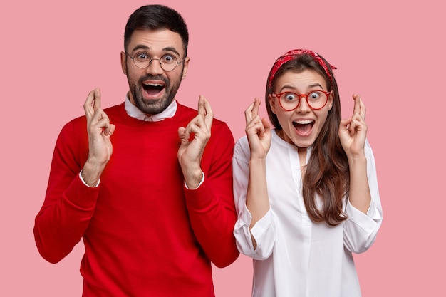 Un jeune couple plein d'espoir prie pour la réalisation de son rêve, levez les mains avec les doigts croisés, espérez et faites un voeu, placez-vous l'un à côté de l'autre