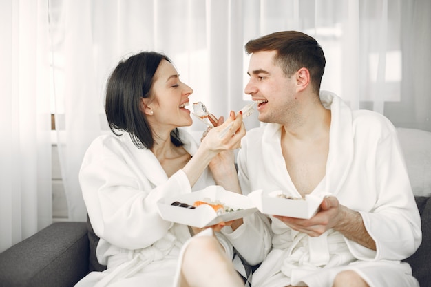 Jeune couple portant des peignoirs, manger des sushis.