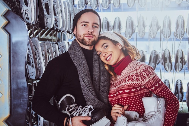 Jeune couple portant des vêtements chauds debout près du rack avec de nombreuses paires de patins, choisissant sa taille