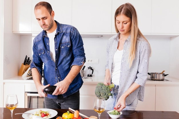 Jeune couple prépare une salade avec des verres à vin sur la table en bois