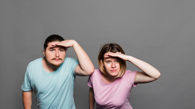 Jeune couple protégeant les yeux avec ses mains sur fond gris