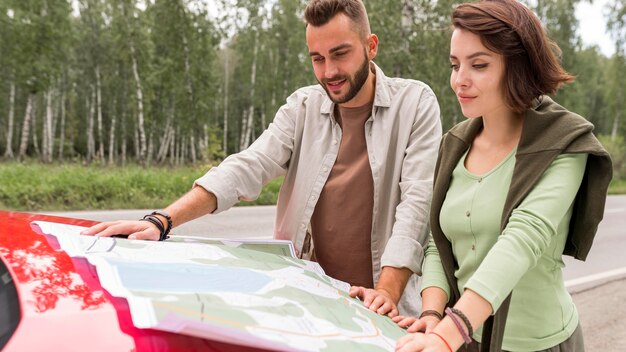 Jeune couple à la recherche sur la carte sur le capot de la voiture