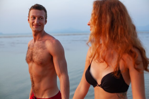 Jeune couple romantique sexy amoureux heureux sur la plage d'été ensemble s'amusant à porter des maillots de bain