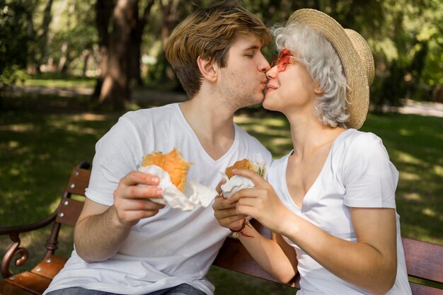 Jeune couple s'embrassant tout en dégustant des hamburgers dans le parc