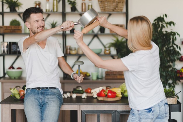 Jeune couple se battant avec une casserole et un rouleau à pâtisserie dans la cuisine