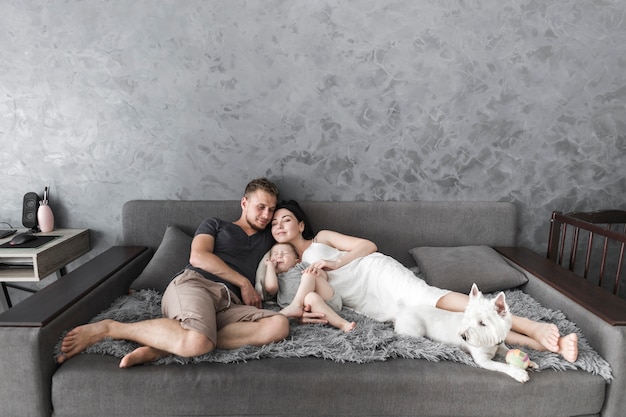 Photo gratuite jeune couple se détendre sur le canapé avec leur fils et chien blanc