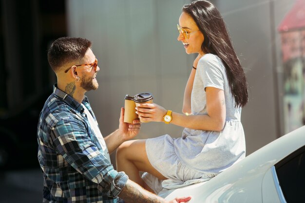 Jeune couple se préparant pour un voyage de vacances sur la voiture en journée ensoleillée. Femme et homme buvant du café et prêts pour la mer ou l'océan.