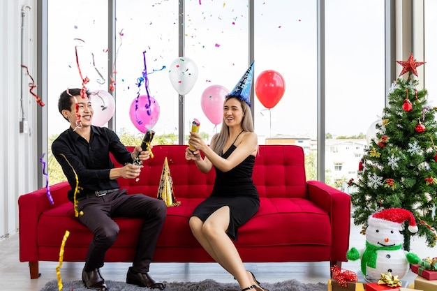 Un jeune couple séduisant célèbre le Nouvel An de Noël avec un popper de fête de confettis et un sapin de Noël décoré et des cadeaux