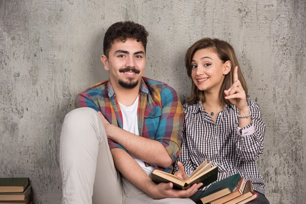 jeune couple souriant assis sur le sol avec des livres