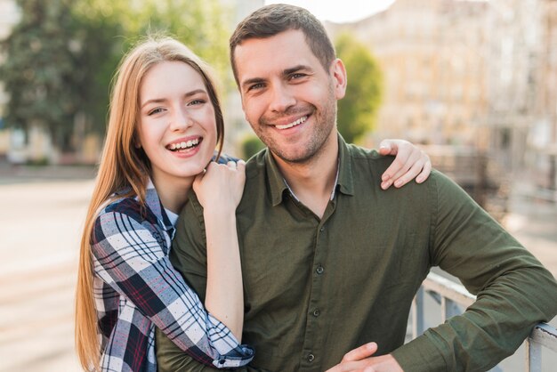 Jeune couple souriant, debout près de la rambarde, regardant la caméra