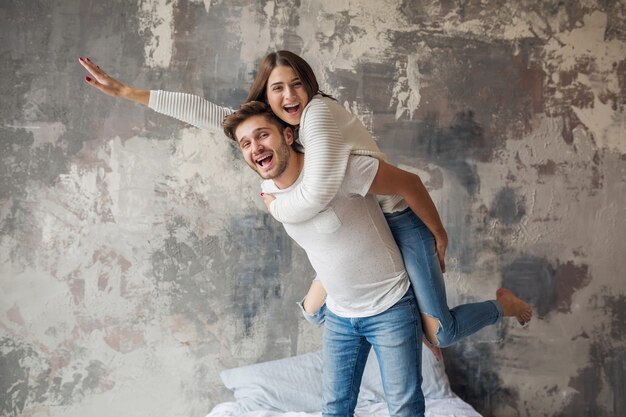 Jeune couple souriant jouant sur le lit à la maison en tenue décontractée, homme et femme s'amusant ensemble, émotion positive folle, heureux, tenant la main