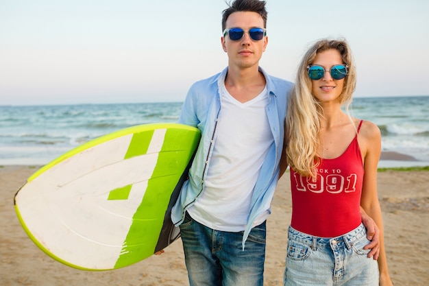 Photo gratuite jeune couple souriant s'amuser sur la plage posant avec planche de surf