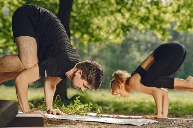 Jeune couple sportif faisant du yoga. Les gens dans un parc d'été.