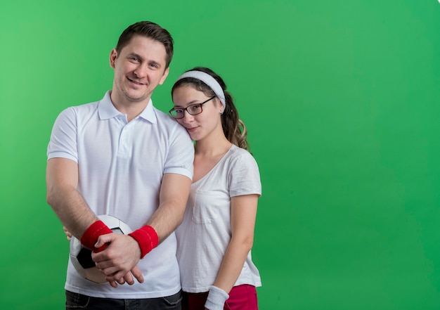 Jeune couple sportif homme et femme debout ensemble souriant heureux et positif sur mur vert