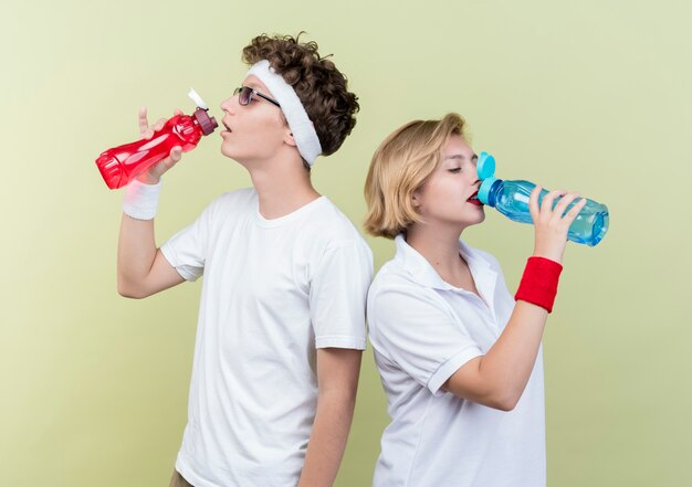 Jeune couple sportif homme et femme de l'eau potable après l'entraînement debout sur un mur léger