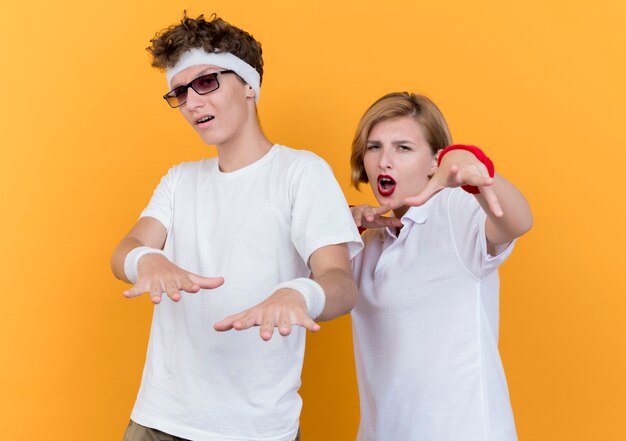 Jeune couple sportif homme et femme avec les mains en souriant s'amuser debout sur un mur orange