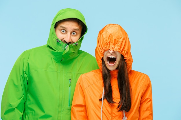 Le jeune couple surpris au studio en vestes d'automne isolé sur bleu.