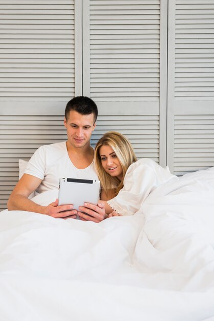 Jeune couple avec tablette sous couverture sur lit