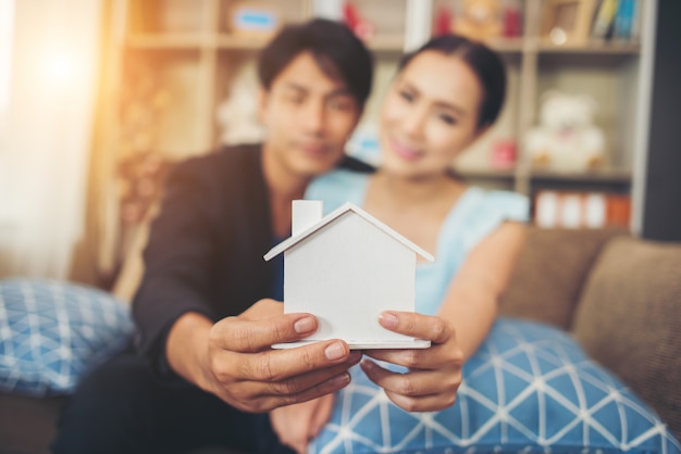 Jeune couple tenant une maison miniature blanche dans le salon