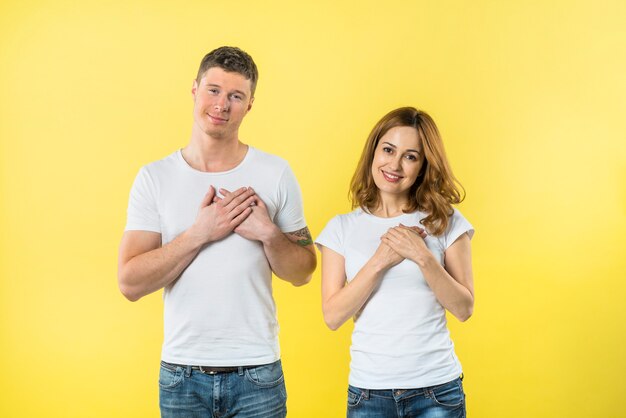 Jeune couple, toucher, leur, cœur, à, deux mains, contre, fond jaune