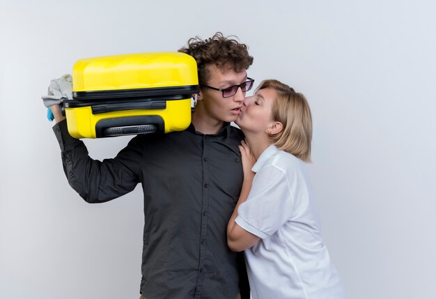 Jeune couple de touristes femme heureuse embrassant son petit ami avec valise debout sur un mur blanc