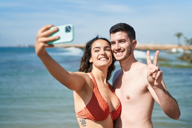 Jeune couple de touristes hispaniques portant un maillot de bain fait selfie par smartphone au bord de la mer