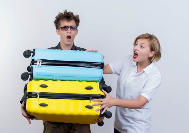 Jeune couple de touristes homme tenant de lourdes valises d'être surpris pendant que sa petite amie essaie d'aider sur blanc