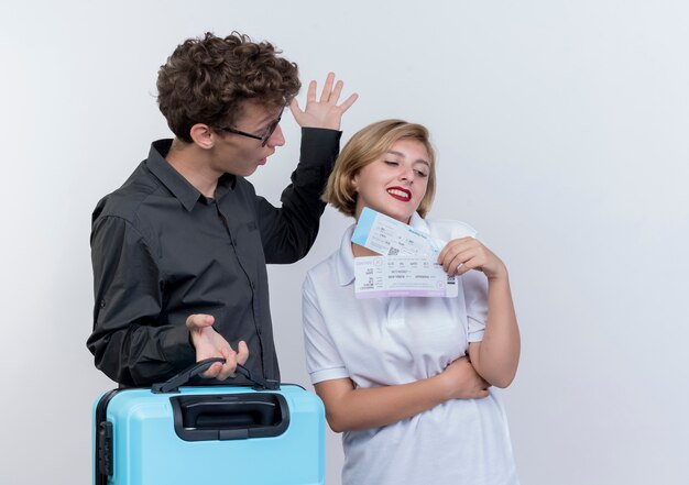 Jeune couple de touristes surpris man holding valise en regardant sa petite amie avec des billets d'avion en mains debout sur un mur blanc