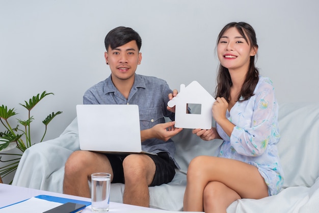 Jeune couple travaille à domicile tandis que la jeune fille tient la maison de papier sur le canapé.