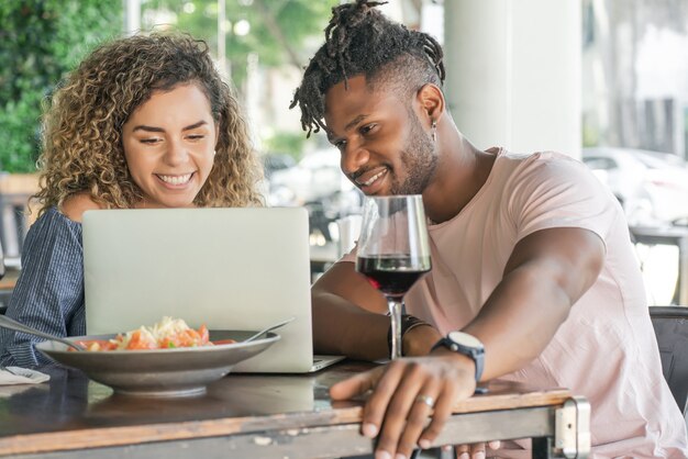 Jeune couple utilisant un ordinateur portable tout en déjeunant ensemble dans un restaurant.