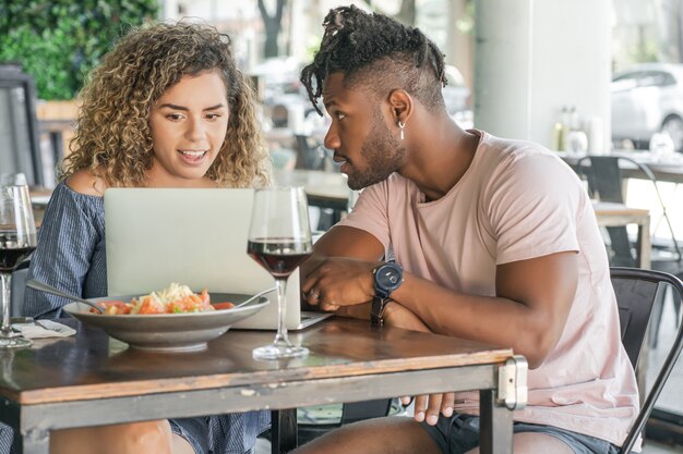 Jeune couple utilisant un ordinateur portable tout en déjeunant ensemble dans un restaurant.