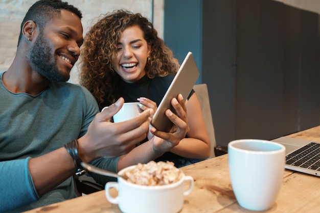 Jeune couple utilisant une tablette numérique tout en prenant le petit déjeuner ensemble à la maison.