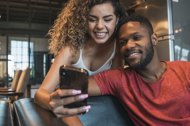 Jeune couple utilisant un téléphone portable assis sur un canapé à la maison.