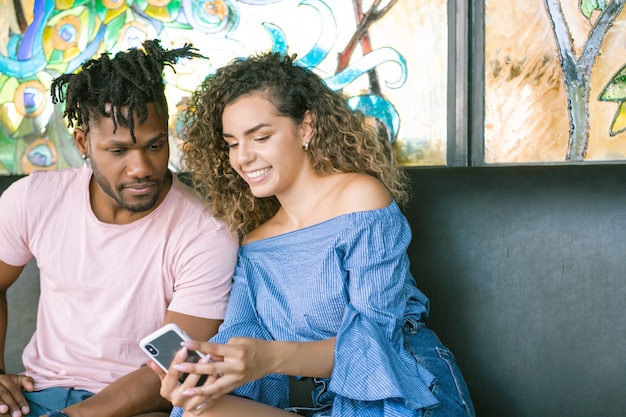 Jeune couple utilisant un téléphone portable et passant du bon temps ensemble dans un restaurant.