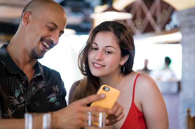 Jeune couple utilisant un téléphone portable tout en profitant d'un rendez-vous ensemble dans un restaurant.