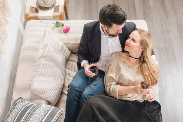 Jeune couple avec des verres de vin assis sur un canapé dans la chambre