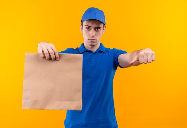 Jeune courrier portant l'uniforme bleu et bonnet bleu faisant des pouces vers le bas tient un sac