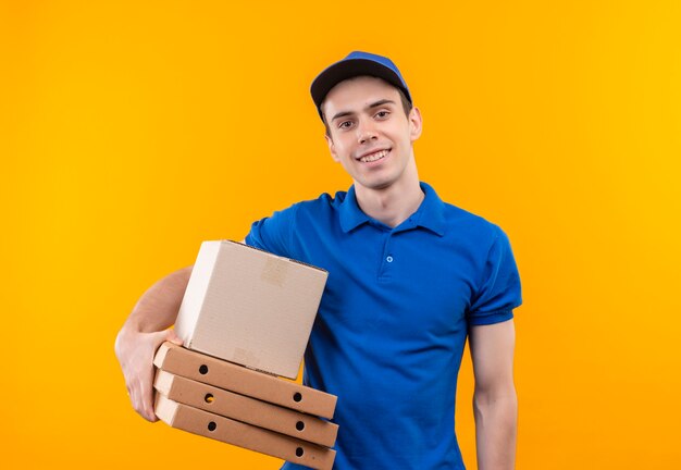 Jeune courrier portant l'uniforme bleu et casquette bleue sourit et détient des boîtes sur la main droite