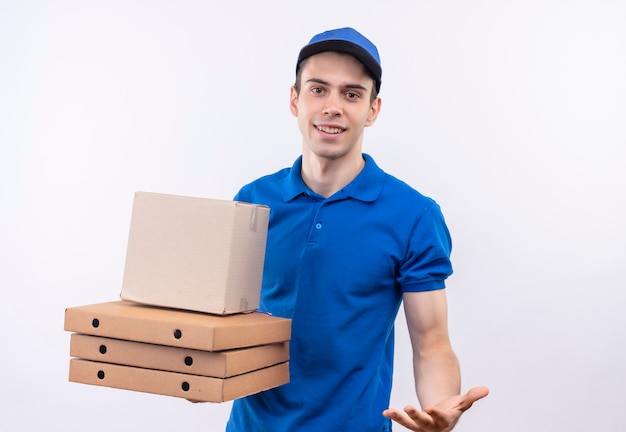 Jeune courrier portant l'uniforme bleu et casquette bleue sourit et détient des boîtes