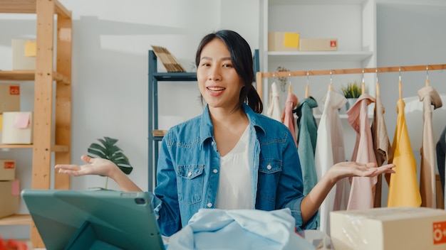 Jeune créateur de mode femme asiatique utilisant un téléphone mobile recevant un bon de commande et montrant des vêtements en streaming