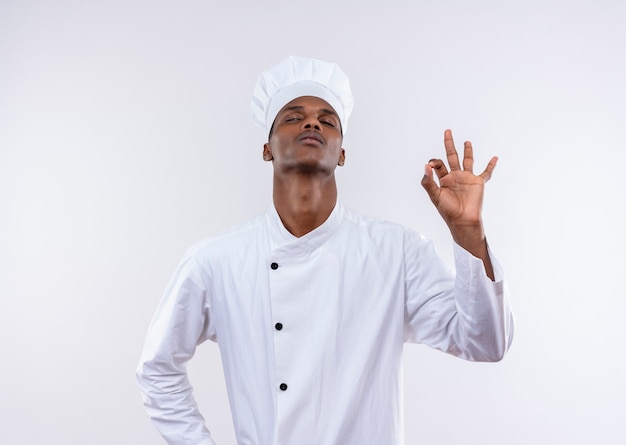 Jeune cuisinier afro-américain confiant dans les gestes uniformes du chef ok avec les yeux fermés isolé sur fond blanc avec espace copie