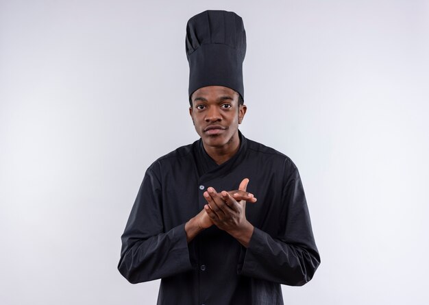 Jeune cuisinier afro-américain confiant en uniforme de chef fait semblant de battre dans ses mains isolé sur fond blanc avec copie espace