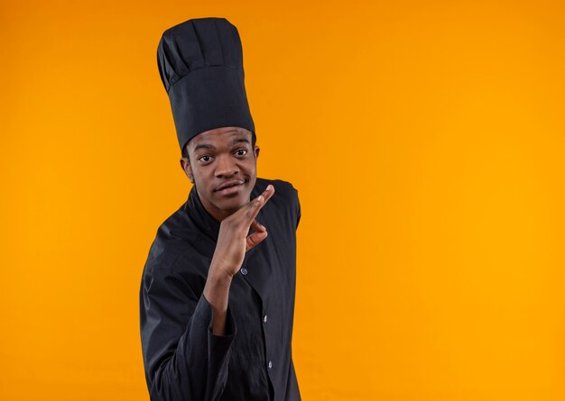 Jeune cuisinier afro-américain confiant en uniforme de chef gestes signe de la main ok isolé sur fond orange avec espace de copie