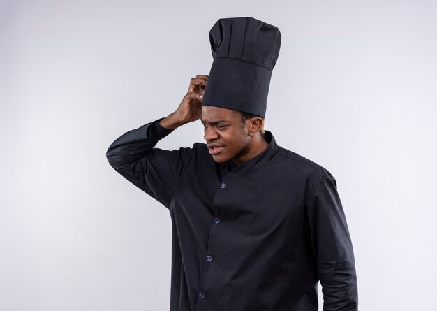 Jeune cuisinier afro-américain confus en uniforme de chef met la main sur la tête isolé sur mur blanc